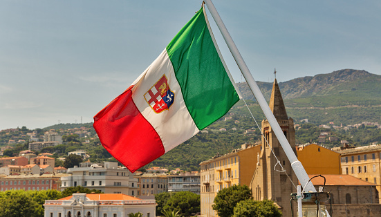 Italian flag closeup with Bastia cityscape in the background. Corsica island, France.