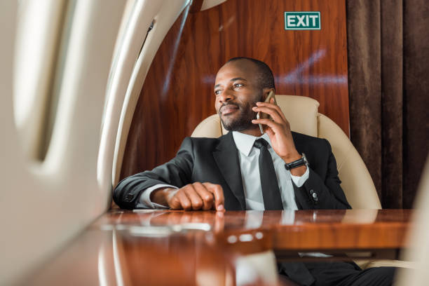 selective focus of handsome african american businessman talking on smartphone in private jet - corporate jet imagens e fotografias de stock