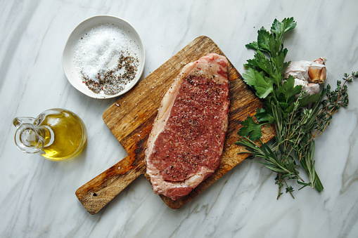 Raw fresh beef steak with ingredients for cooking on light background