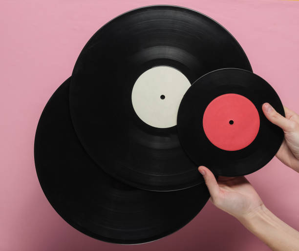 istock Female hands hold a vinyl record on a pink pastel background. Top view 1194266881