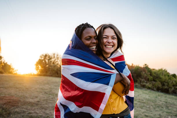 Two multi-ethnic women holding British flag Two young pretty multi-ethnic women holding British flag on meadow. british flag photos stock pictures, royalty-free photos & images