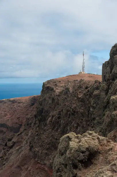 Cellphone radiomast on a high rock on a blue sea and cloudy sky background.