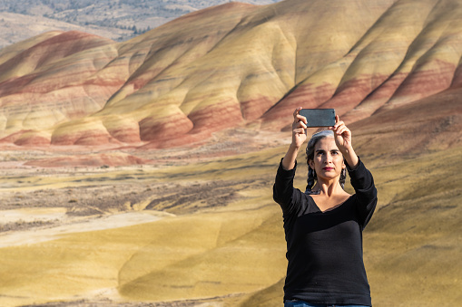 A young brunette with gray strands takes selfies at Painted Hills Overlook, Oregon, USA.