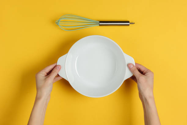istock Female hands hold an empty ceramic bowl on a yellow background with whisks. Top view 1194271977