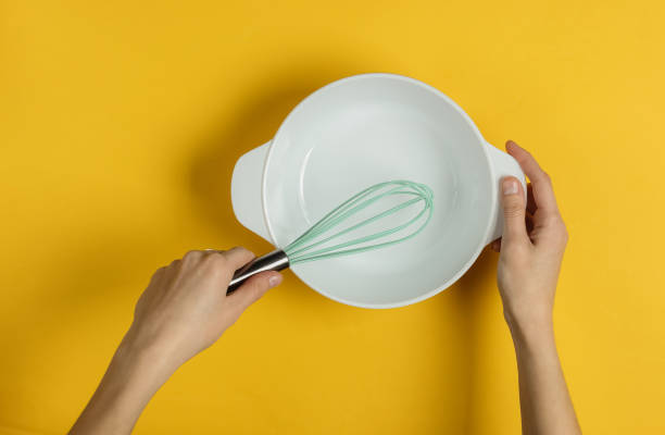 istock Female hands holding empty ceramic bowl and whisk on a yellow background. Top view 1194272016