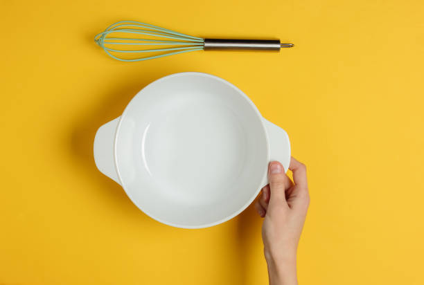 istock Female hands hold an empty ceramic bowl on a yellow background with whisks. Top view 1194272017
