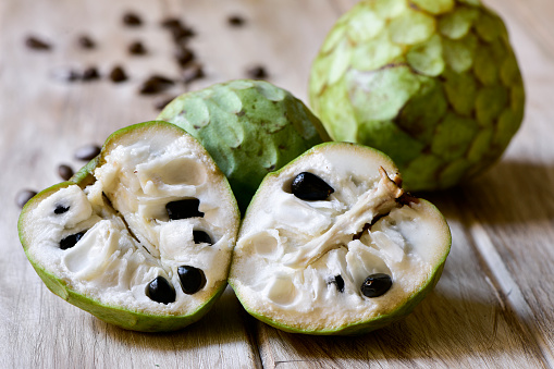 closeup of some custard apples, one of them cut in half, on a rustic wooden surface