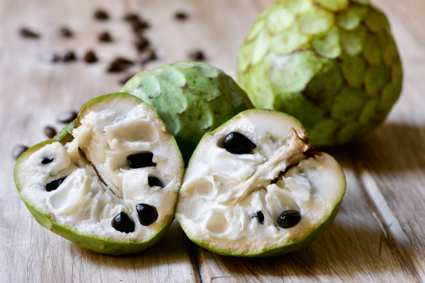 custard apples on a wooden surface closeup of some custard apples, one of them cut in half, on a rustic wooden surface annonaceae stock pictures, royalty-free photos & images