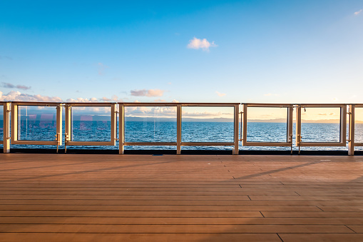 Safety railing and wooden deck of cruise ship. Vessel sailing on the Caribbean Sea. Sunset time. Blue sky and some clouds. Space for copy. Horizontal lines.