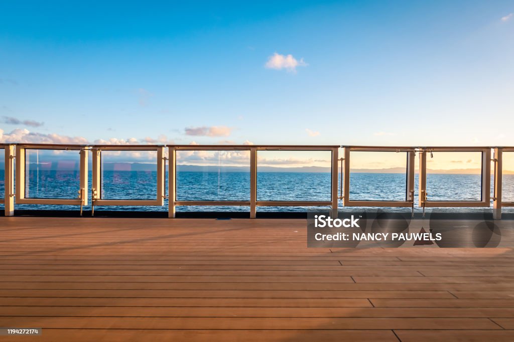 Cruise ship deck view. Safety railing and wooden deck of cruise ship. Vessel sailing on the Caribbean Sea. Sunset time. Blue sky and some clouds. Space for copy. Horizontal lines. Cruise Ship Stock Photo