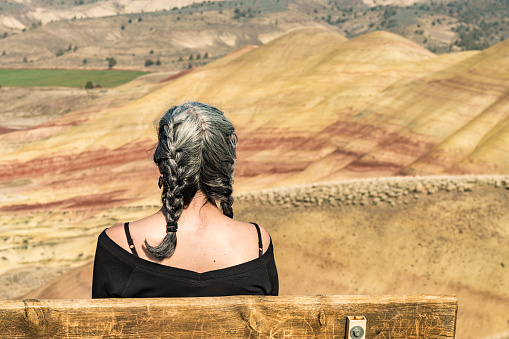 A young brunette with gray strands enjoys the view from a bench in Painted Hills Overlook, Oregon, USA.