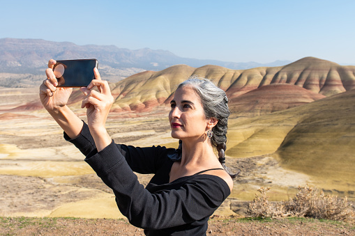 A young brunette with gray strands takes selfies at Painted Hills Overlook, Oregon, USA.