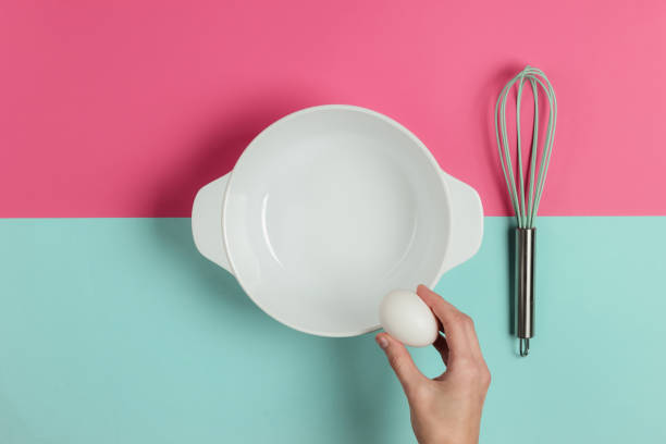 istock Female hand breaks a chicken egg on a ceramic bowl on a blue-pink studio background. Top view 1194273605