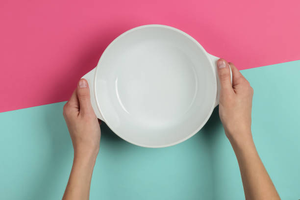 istock Female hands hold empty ceramic bowl pink blue background. Top view 1194273620