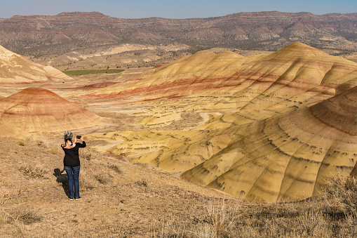 A young brunette with gray hair takes pictures with her smartphone in Painted Hills Overlook, Oregon, USA.