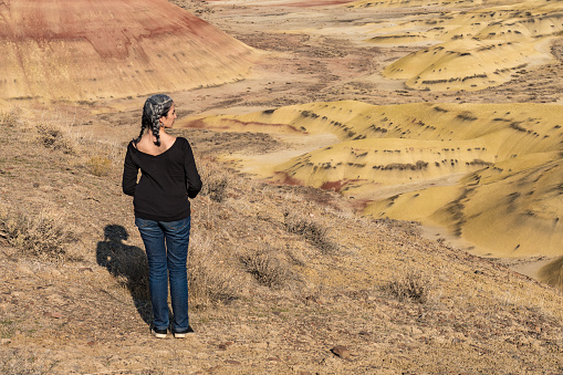 A young brunette with gray strands observes the landscape from Painted Hills Overlook, Oregon, USA.