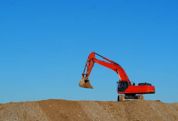 istock Orange excavator between a dune of dirt and cloudless sky. 1194277916