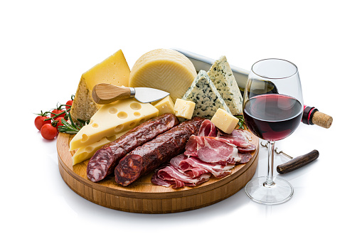 Cheese and wine: high angle view of a cutting board with various cheese slices, Serrano ham and spanish chorizo isolated on white background. A red wine bottle and a wineglass are behind the cheese platter. Useful copy space available for text and/or logo. High resolution 42Mp studio digital capture taken with Sony A7rii and Sony FE 90mm f2.8 macro G OSS lens