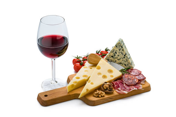 Cheese and wine: high angle view of a cutting board with various cheese slices, Serrano ham and spanish chorizo isolated on white background. A red wineglass is beside the cheese board. Useful copy space available for text and/or logo. High resolution 42Mp studio digital capture taken with Sony A7rii and Sony FE 90mm f2.8 macro G OSS lens