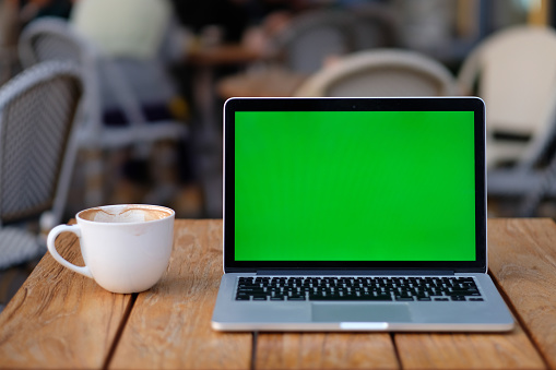 close up one green screen laptop computer on wooden table with a cup of coffee.