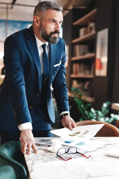 istock Stylish businessman standing near table in the office and reading documents 1194285667