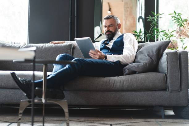 istock smiling businessman with digital tablet sitting on sofa 1194285713