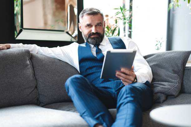 istock smiling businessman with digital tablet sitting on sofa 1194285719