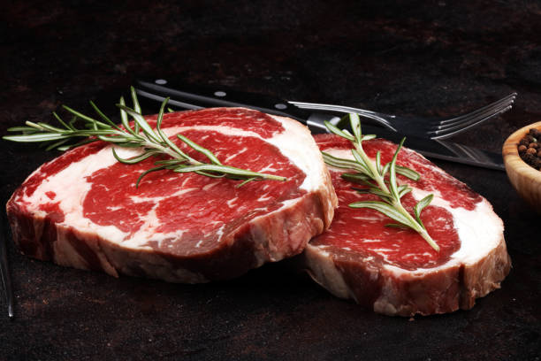 Raw fresh meat Ribeye Steak, seasoning and meat fork on rustic background