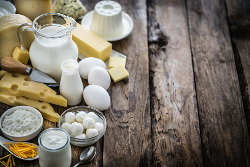 High angle view of a large assortment of most common dairy products shot on rustic wooden table. The composition is at the left of an horizontal frame and includes milk, sour cream, butter, yogurt, eggs, goat cheese, emmental cheese, Cheddar cheese, Roquefort cheese and cottage cheese. Some cheeses are on a wooden cutting board. Predominant colors are white, yellow and brown. High resolution 42Mp studio digital capture taken with Sony A7rii and Sony FE 90mm f2.8 macro G OSS lens