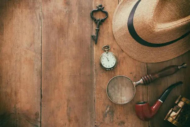 Concept image of investigation or private detective. Fedora hat, magnifing glass and vintage items over wooden table