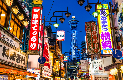 The brightly colour neon lights and noisy cityscape of Shinsekai overlooked by the iconic tower of Tsutenkaku in the heart of Osaka, Japan's vibrant second city.