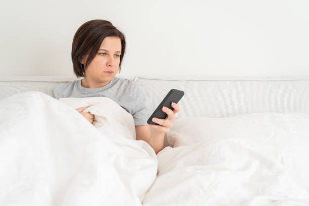 istock Woman using smartphone as she sits in bed covered with duvet 1194294478