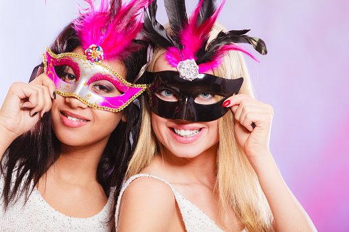 Holidays, people and celebration concept. two women mixed race and caucasian with carnival venetian masks over festive background.