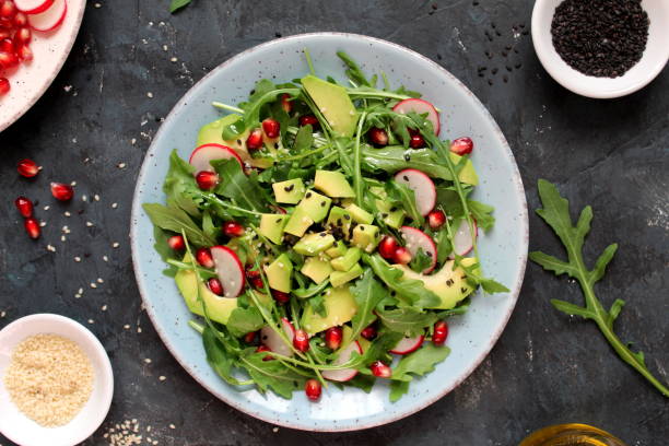 istock Ingredient for making salad on dark background. Vegetables salad in plate: avocado, arugula, pomegranate, radish and sesame. 1194300592