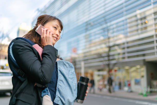 multitarefa mãe trabalhadora pendulares enquanto carregava seu bebê e fala no smartphone - rush hour commuter on the phone tokyo prefecture - fotografias e filmes do acervo