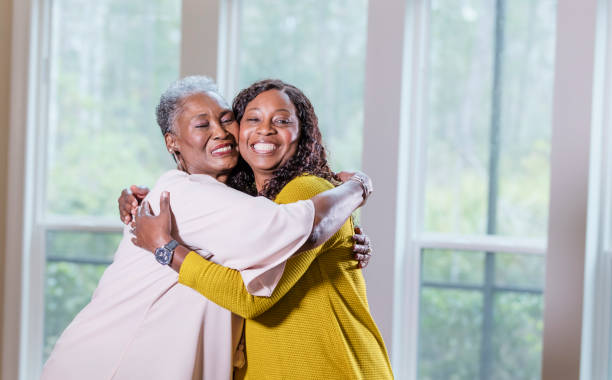 Senior African-American woman, adult daughter hugging A senior African-American woman in her 70s hugging her adult daughter, a mature woman in her 50s. They are smiling and looking toward the camera. cheek to cheek photos stock pictures, royalty-free photos & images