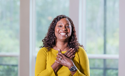 Portrait of a mature African-American woman in her 50s wearing a yellow sweater, smiling at the camera.