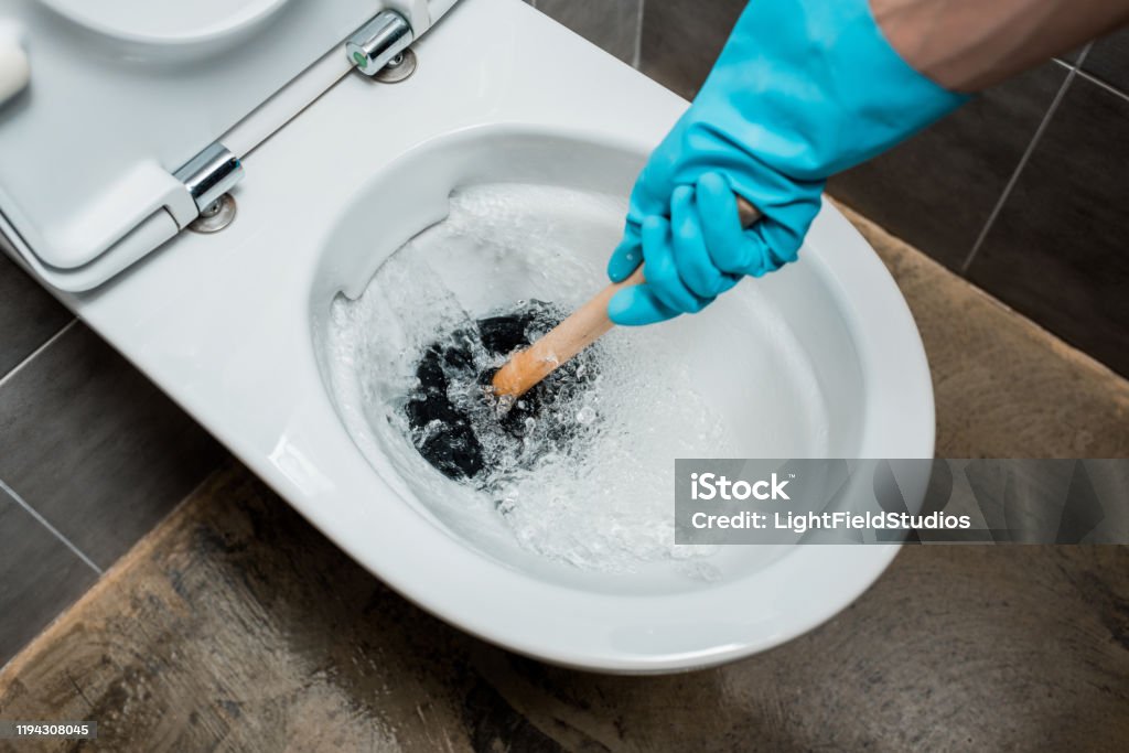 cropped view of plumber using plunger in toilet bowl during flushing in modern restroom with grey tile Plunger Stock Photo cropped view of plumber using plunger in toilet bowl during flushing in modern restroom with grey tile Plunger Stock Photo