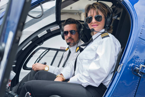 istock Black-haired man with a beard of approximately 40 years dressed in his pilot uniform accompanied by a blue helicopter cockpit, his co-pilot Latin woman with short blond hair and pilot uniform is soon to take off 1194308384