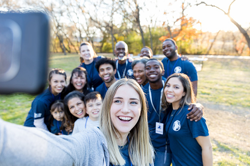 Happy group of diverse neighbors take a selfie after successfully cleaning up their neighborhood.