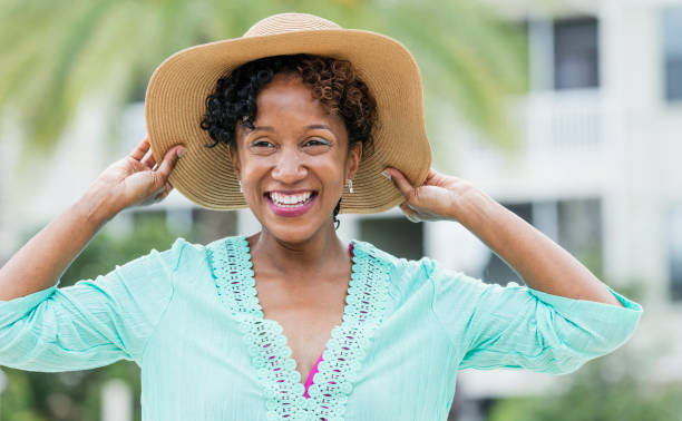 Mature African-American woman wearing sun hat A mature African-American woman in her 40s having fun on vacation. She is wearing a wide brim sun hat, laughing, looking away from the camera. sun hat stock pictures, royalty-free photos & images