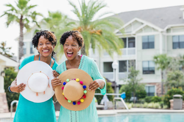 istock Identical twins standing by pool, holding sun hats 1194311177