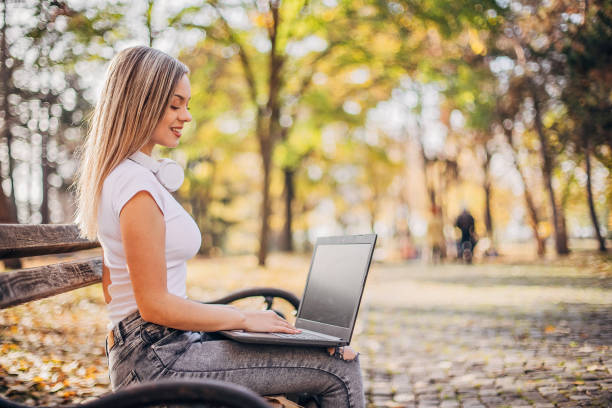 istock Young woman is sitting on a park bench and using laptop 1194311660