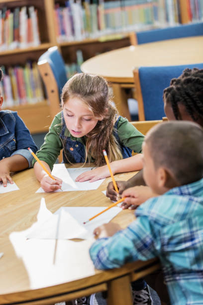 istock Elementary school girl and classmates writing on paper 1194314856