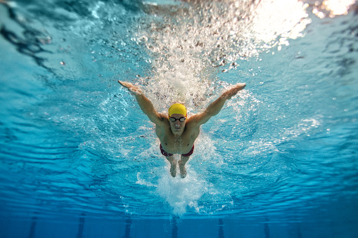 Underwater shot of young man practicing butterfly stroke style of swimming in the swimming pool.