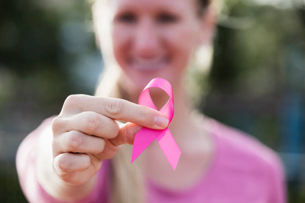 Young woman in pink with breast cancer awareness ribbon A young woman in her 20s smiling, wearing a pink shirt, hopeful as she holds a breast cancer awareness ribbon. The focus is on her hand and the ribbon. brest cancer hope stock pictures, royalty-free photos & images