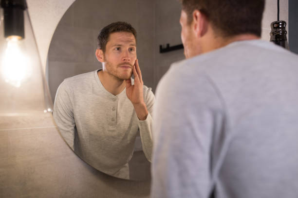 istock Man looking at himself in the mirror and touching his face 1194318229