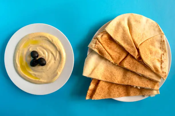 Photo of Tahini sauce with pita bread on blue background.