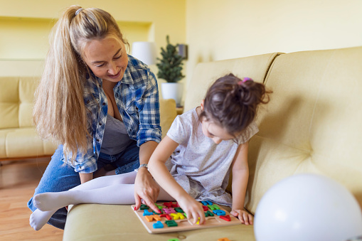 A young single mother is helping her cute little daughter with alphabet learning. Mother is giving her daughter a lesson with an alphabet therapy exercise.