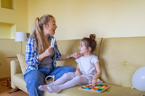 A young single mother is helping her cute little daughter with alphabet learning. Mother is giving her daughter a lesson with an alphabet therapy exercise.